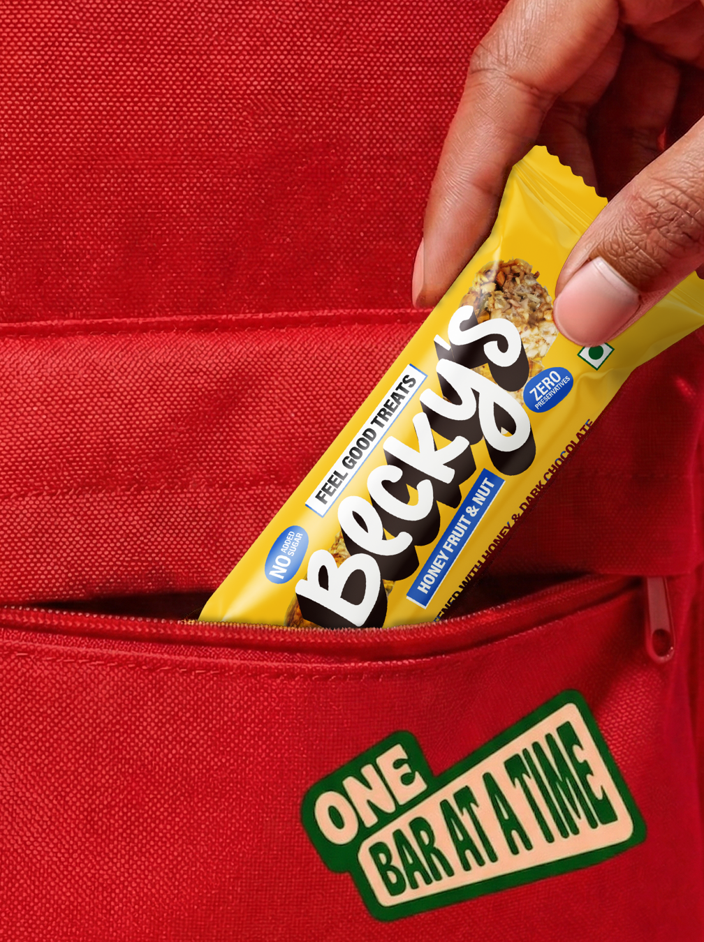Hand holding a Becky's snack bar in front of a red bag with branding text.